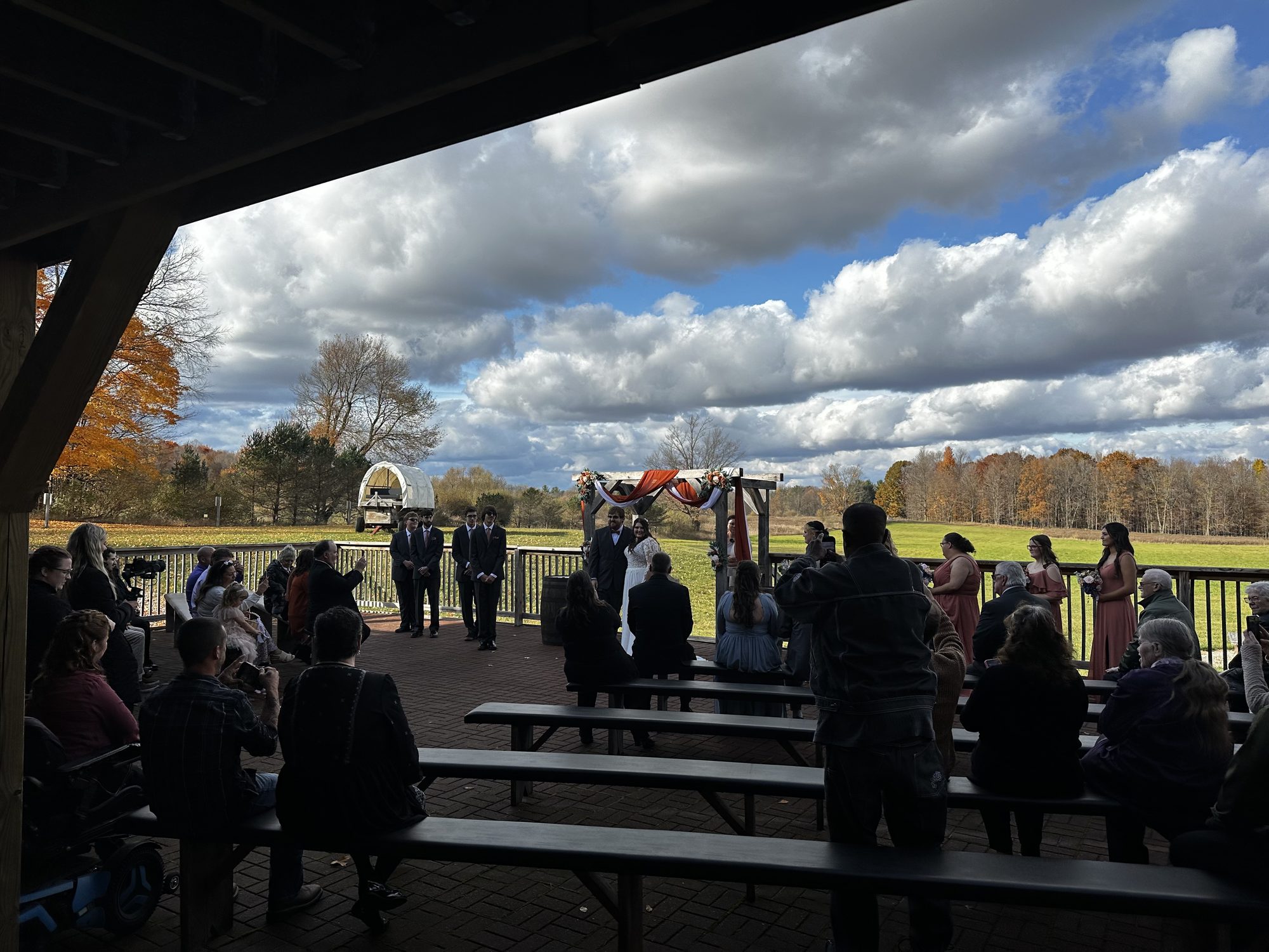 Guests watching an outdoor ceremony from beneath a barn pavilion