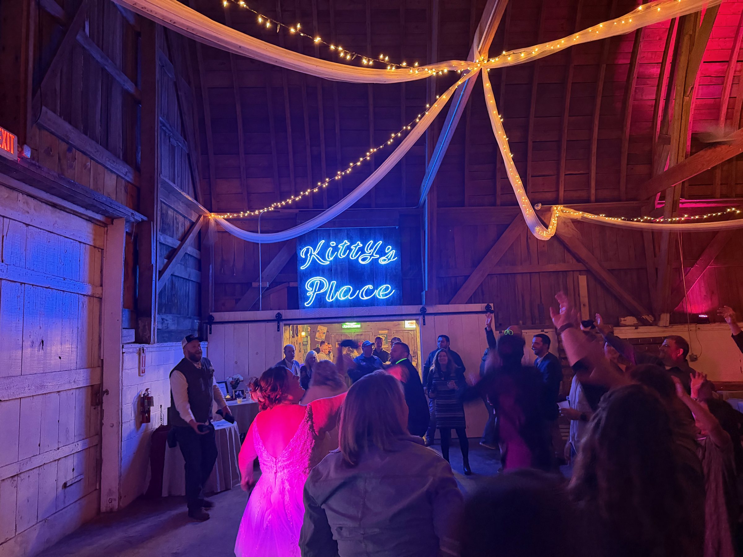 Wedding guests celebrating beneath colorful lights in a decorated barn