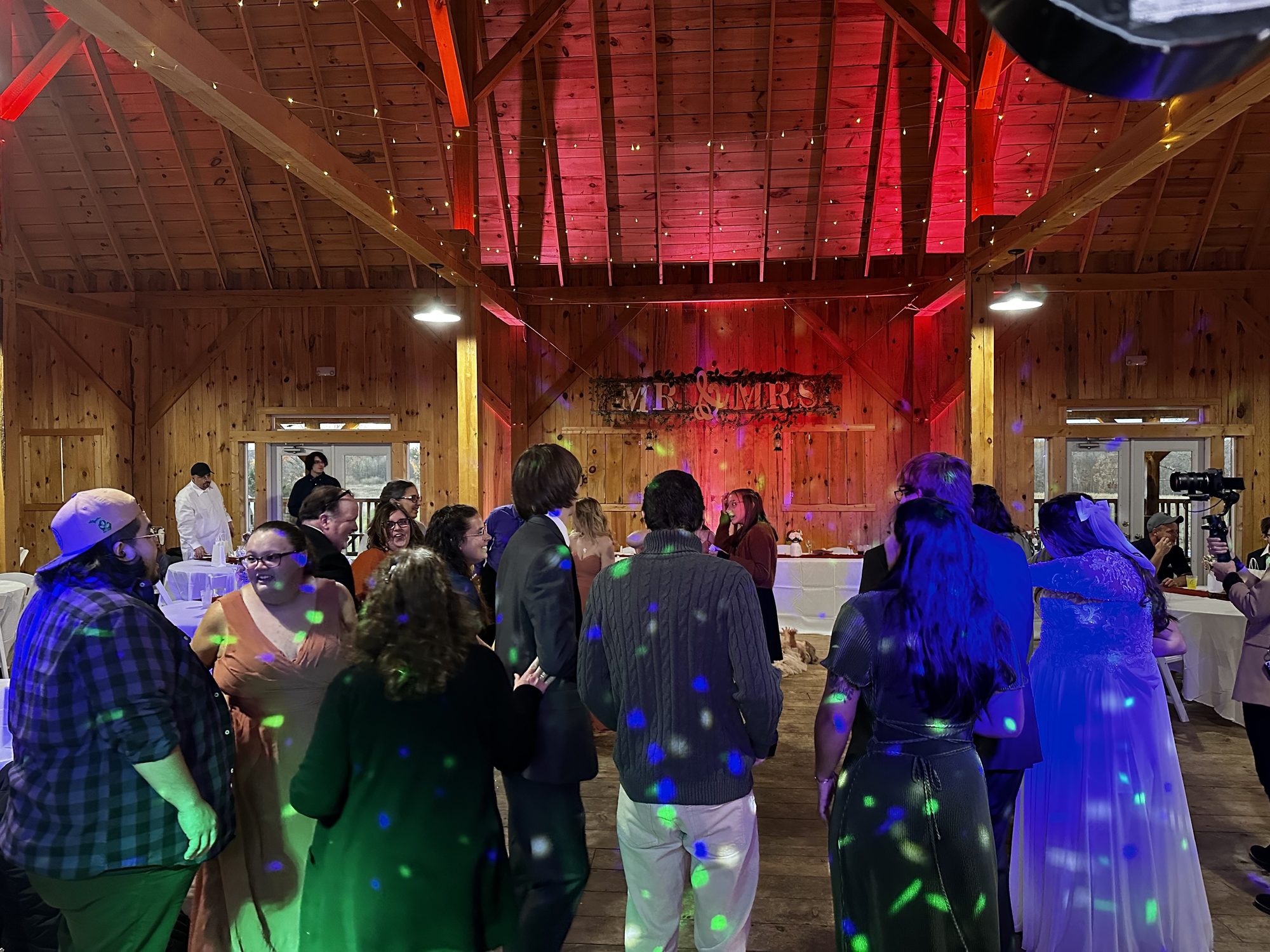 Wedding guests dancing beneath colorful dots in a wooden barn