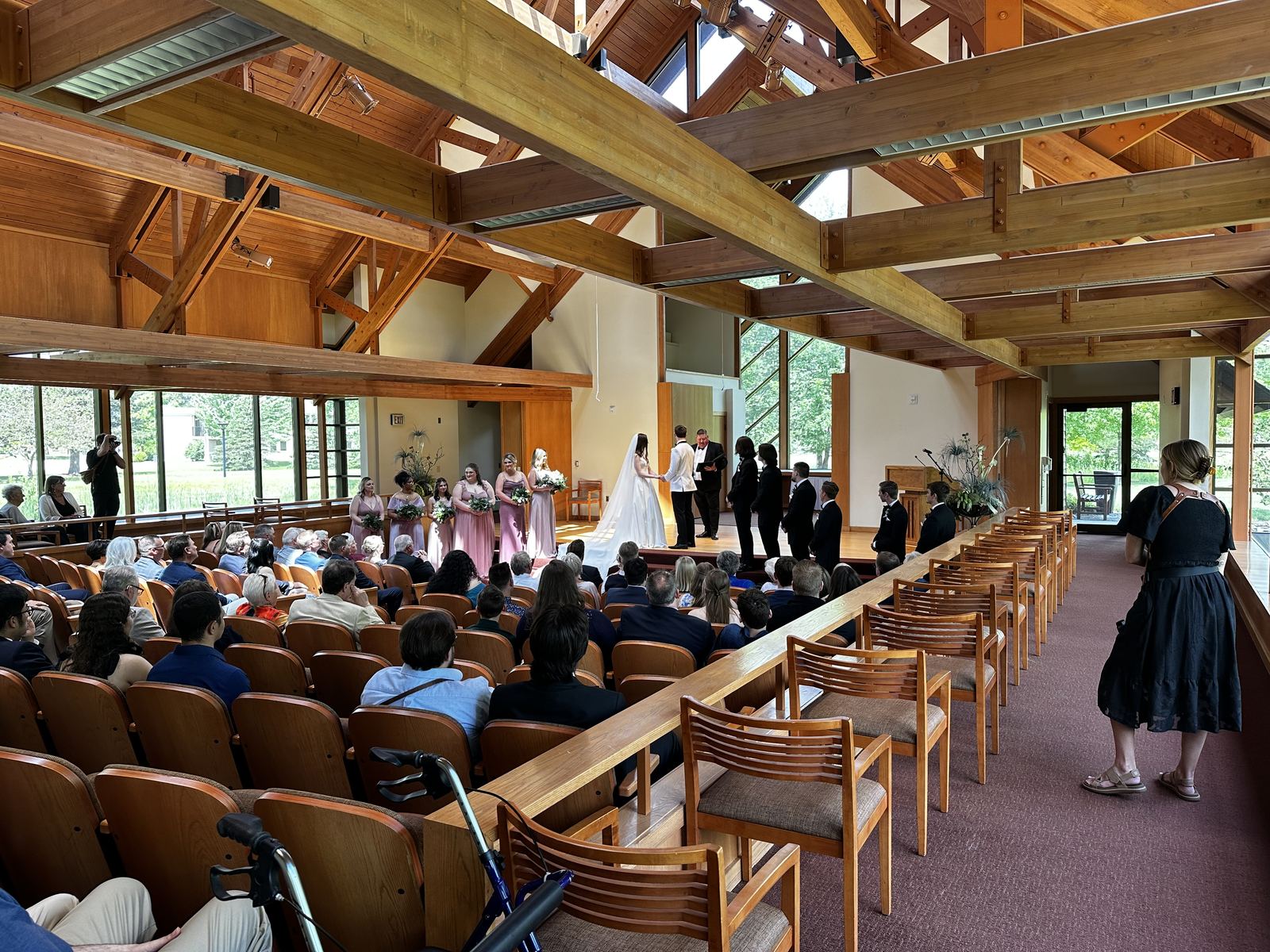 Wedding ceremony viewed down the aisle of a bright wooden chapel