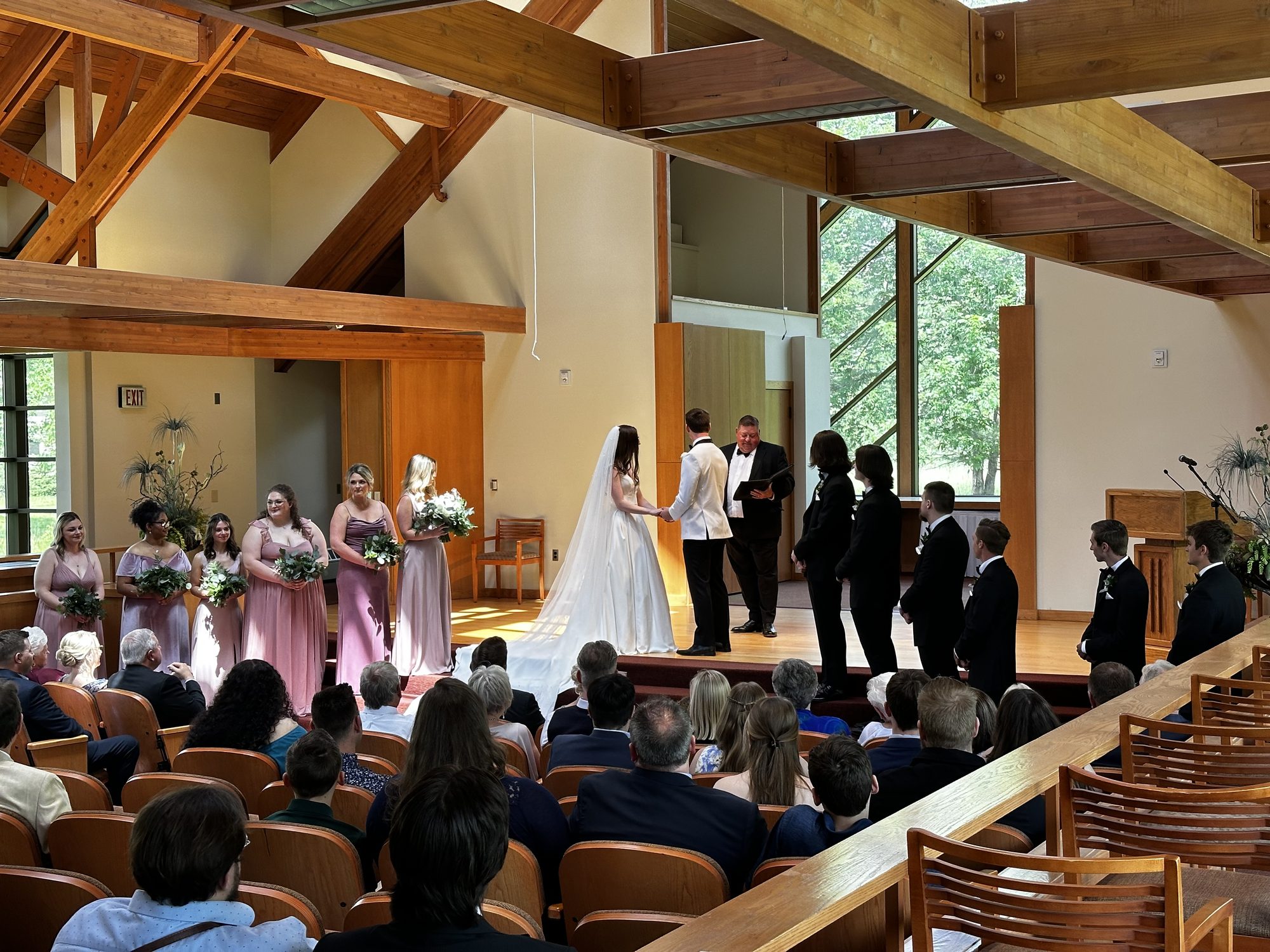 Wedding party gathered at the front of a bright wooden chapel