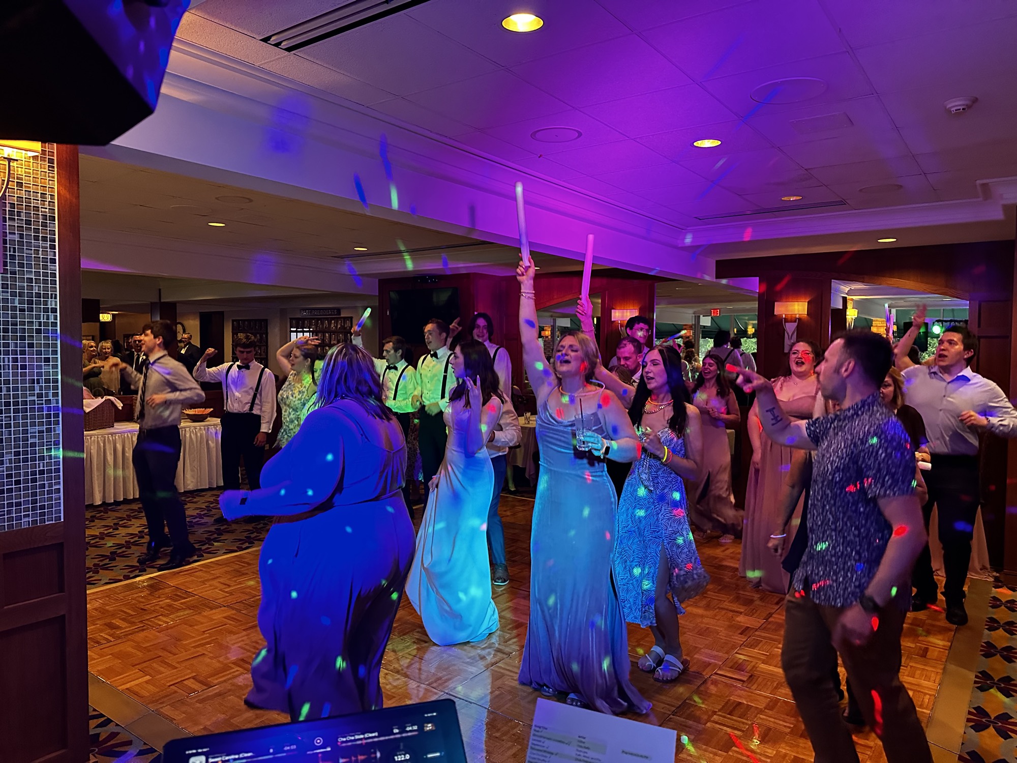 A packed wedding crowd dancing beneath vivid party lighting