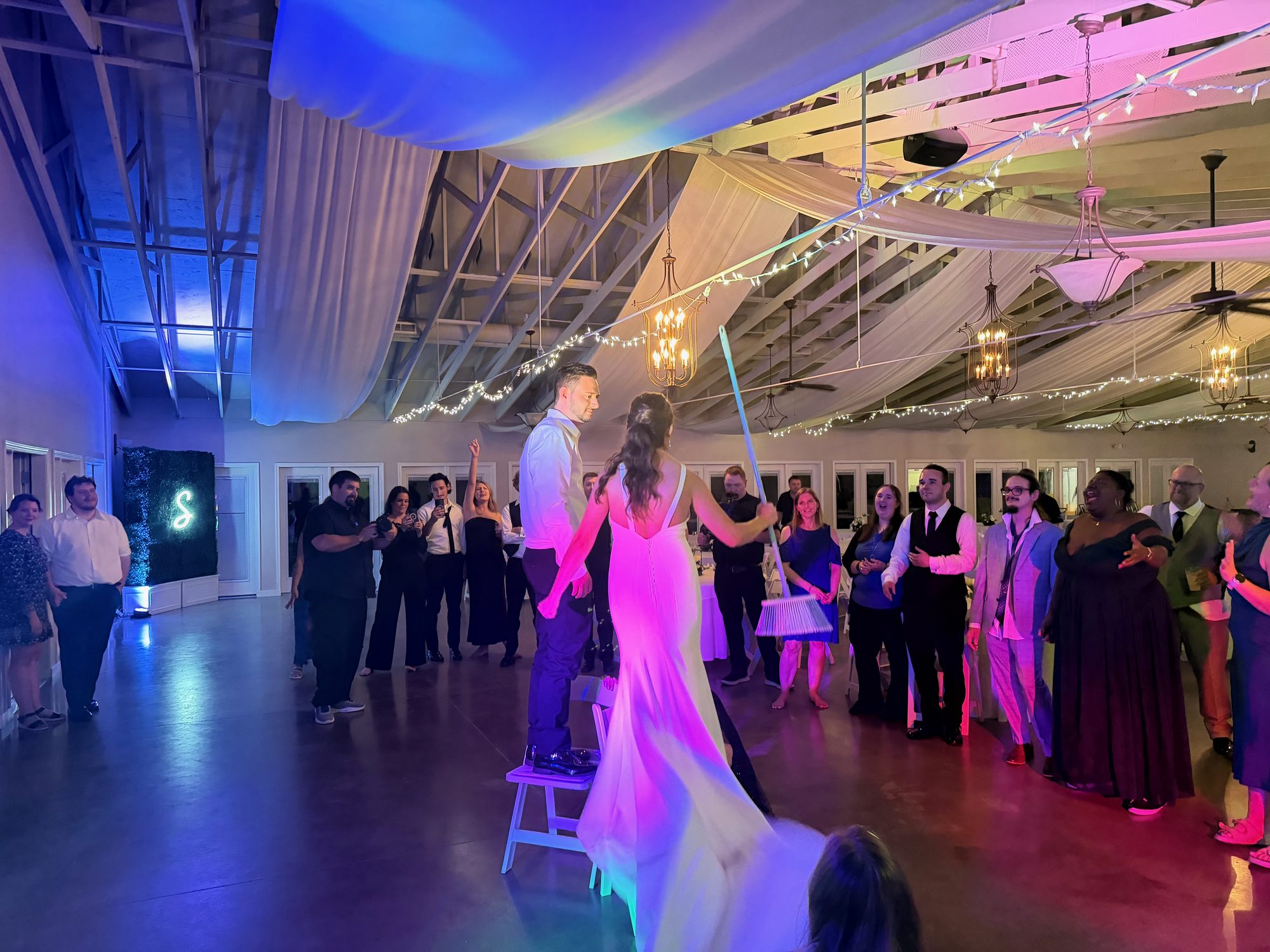 A bride dancing with guests beneath colorful reception lighting