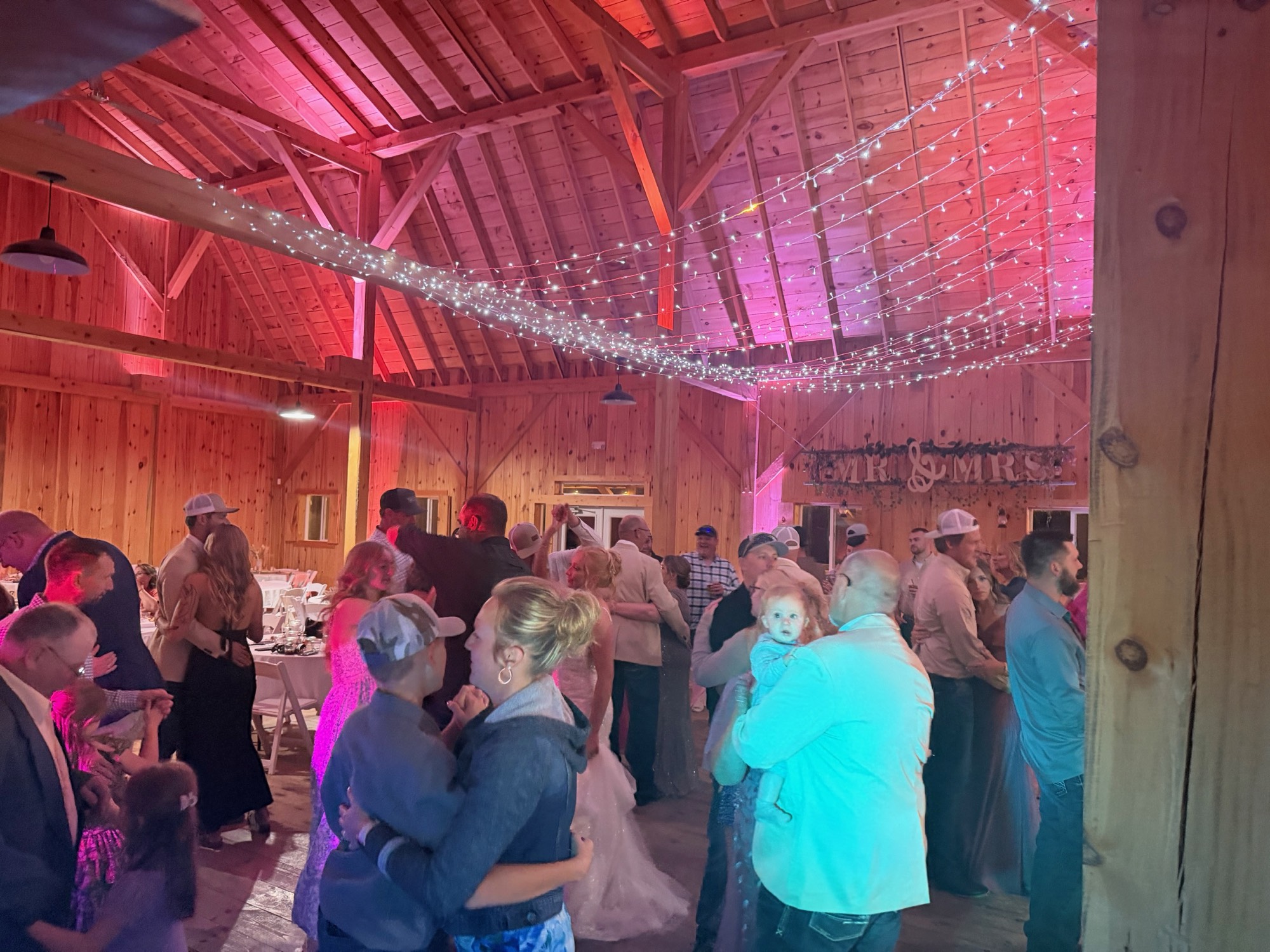 A full barn reception dance floor beneath string lights and red uplighting
