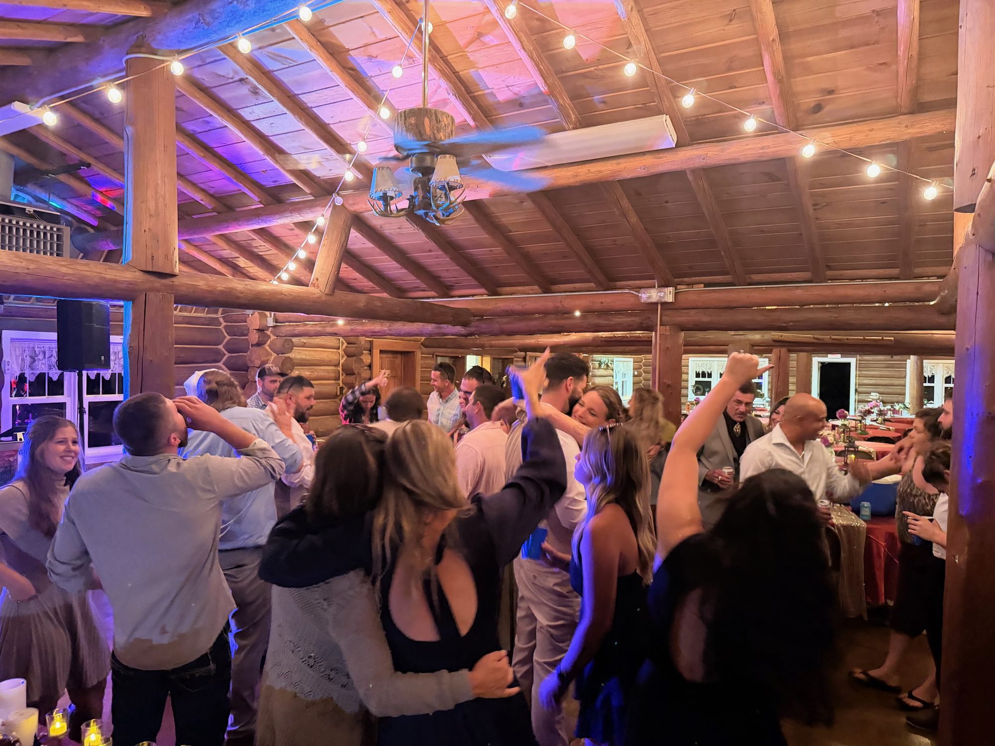 A tightly packed rustic wedding dance floor with hands in the air
