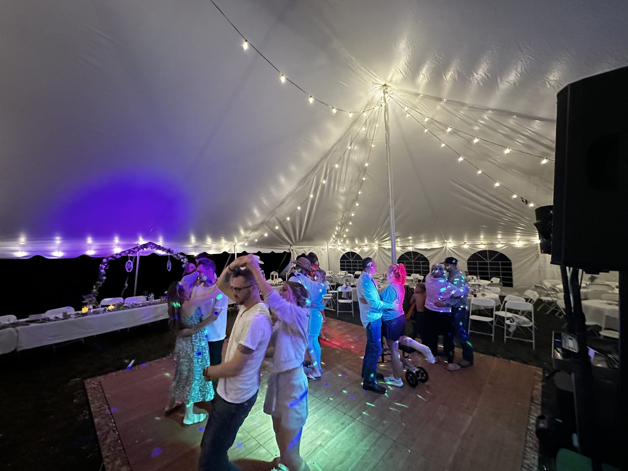 Wedding guests dancing beneath string lights and colorful party lighting