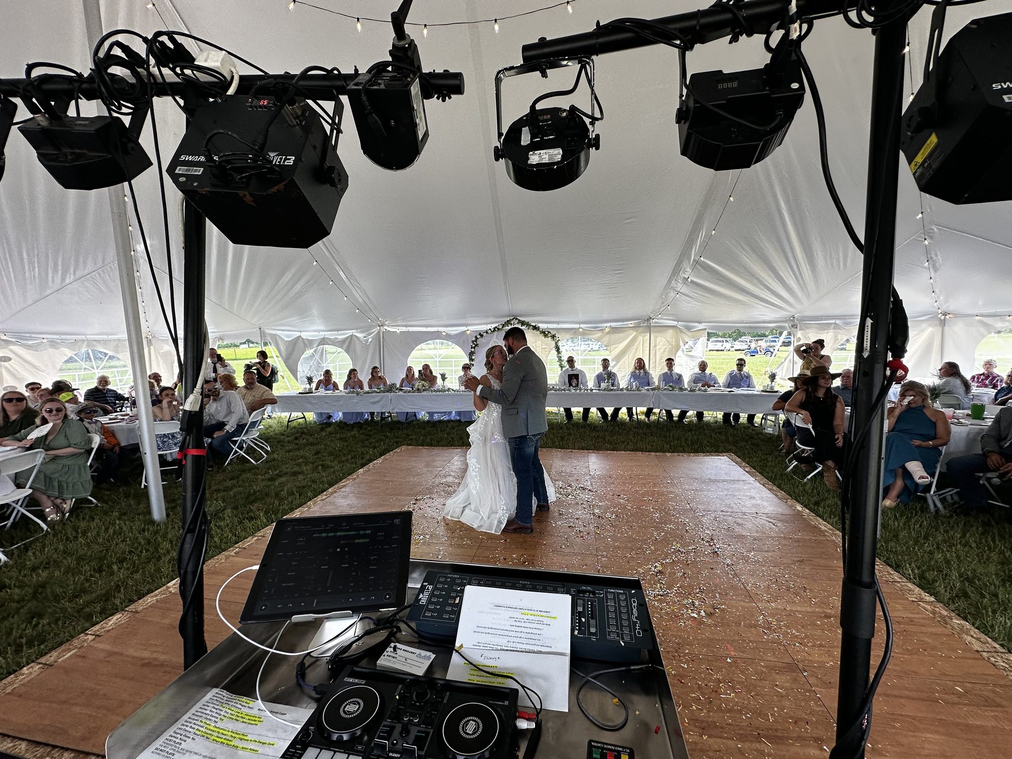 Newlyweds sharing a first dance beneath a tent from the DJ viewpoint