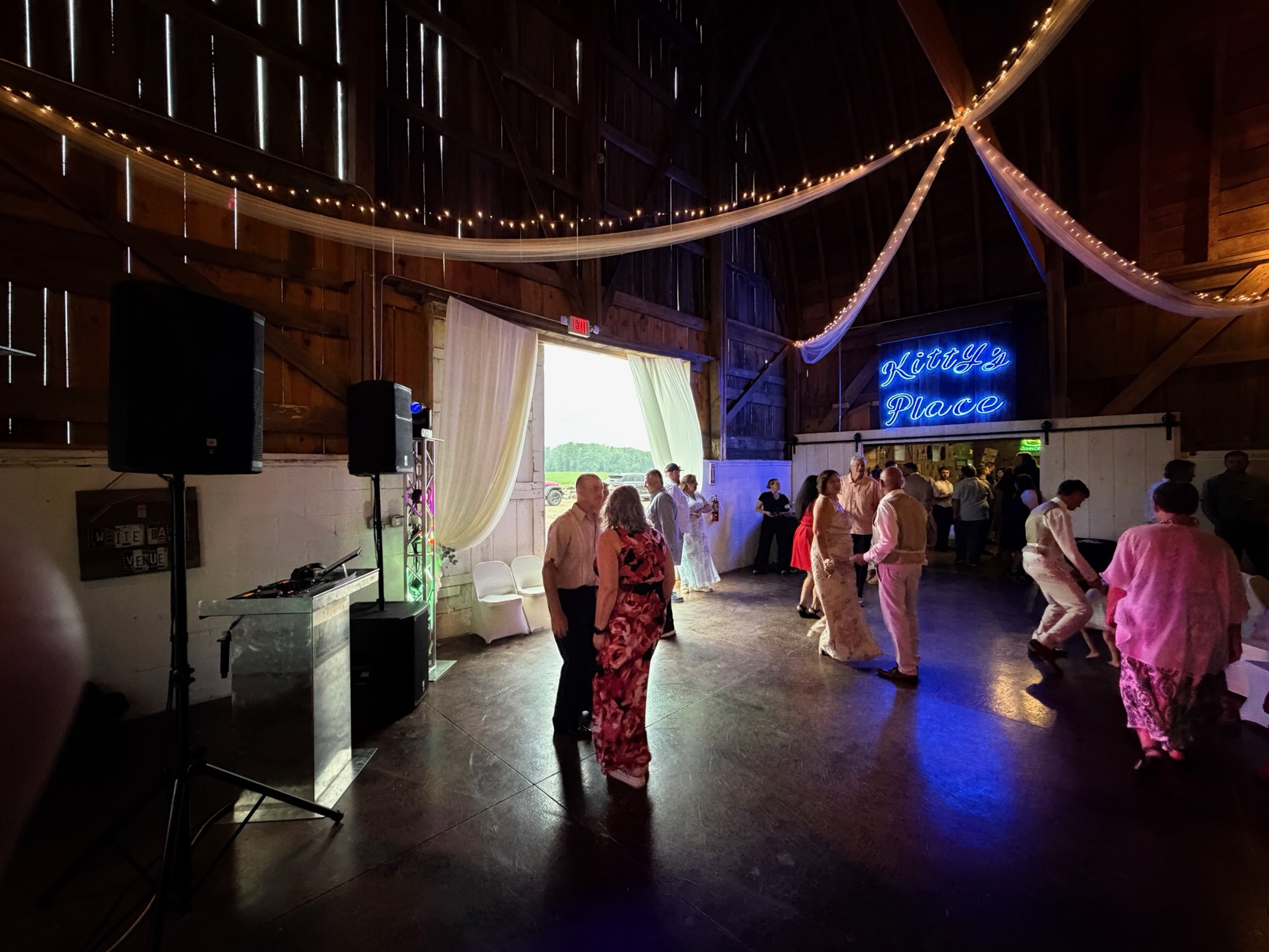 NewAge DJ equipment and lighting beside guests dancing in a barn venue