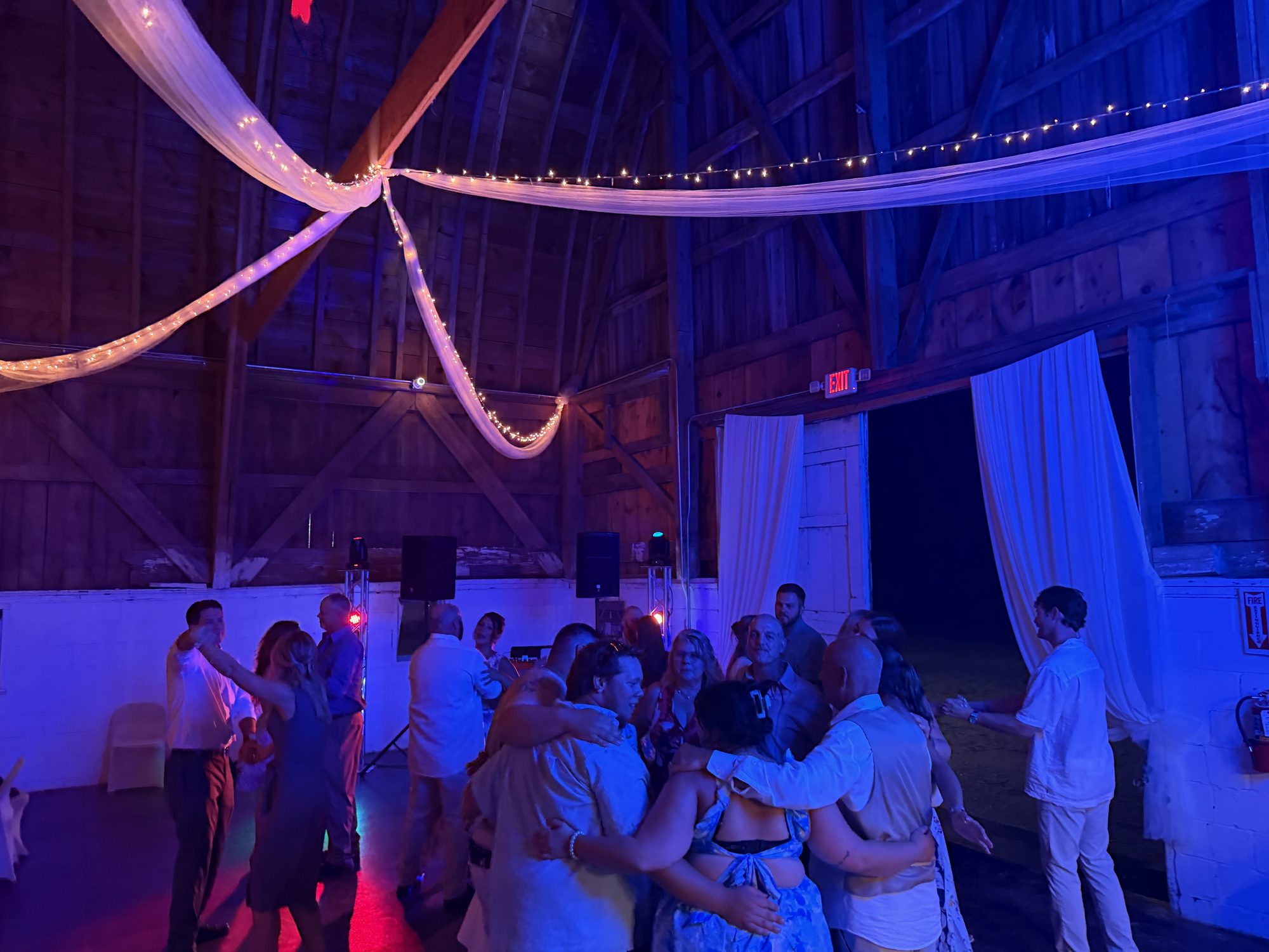 A large group of wedding guests dancing together in a barn