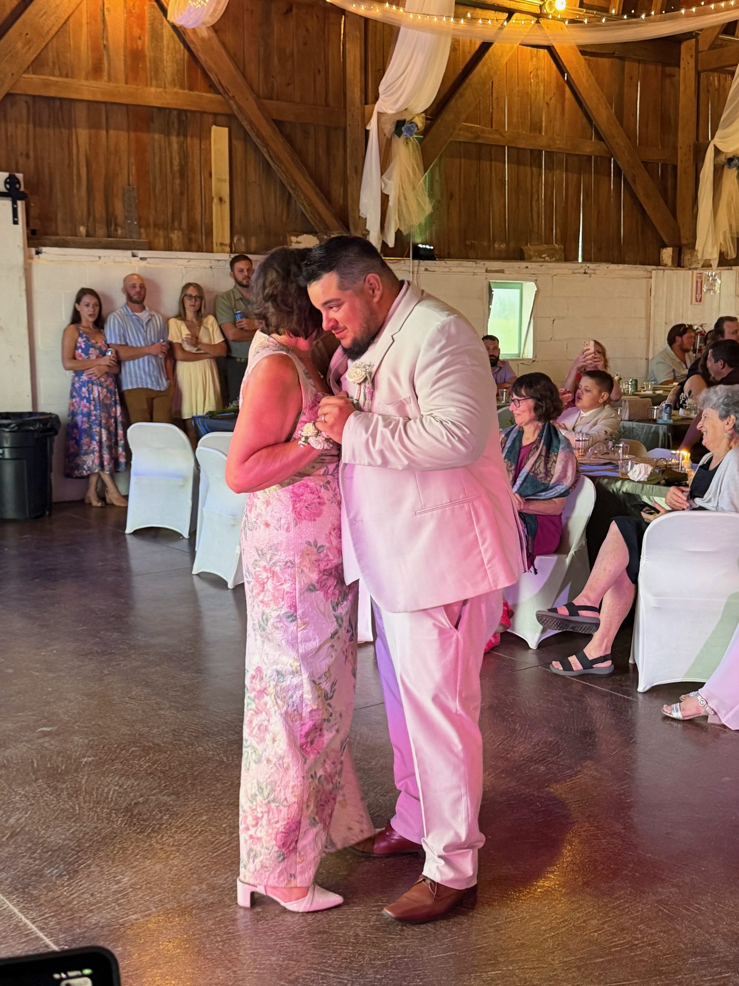 A groom sharing a parent dance at a rustic wedding reception